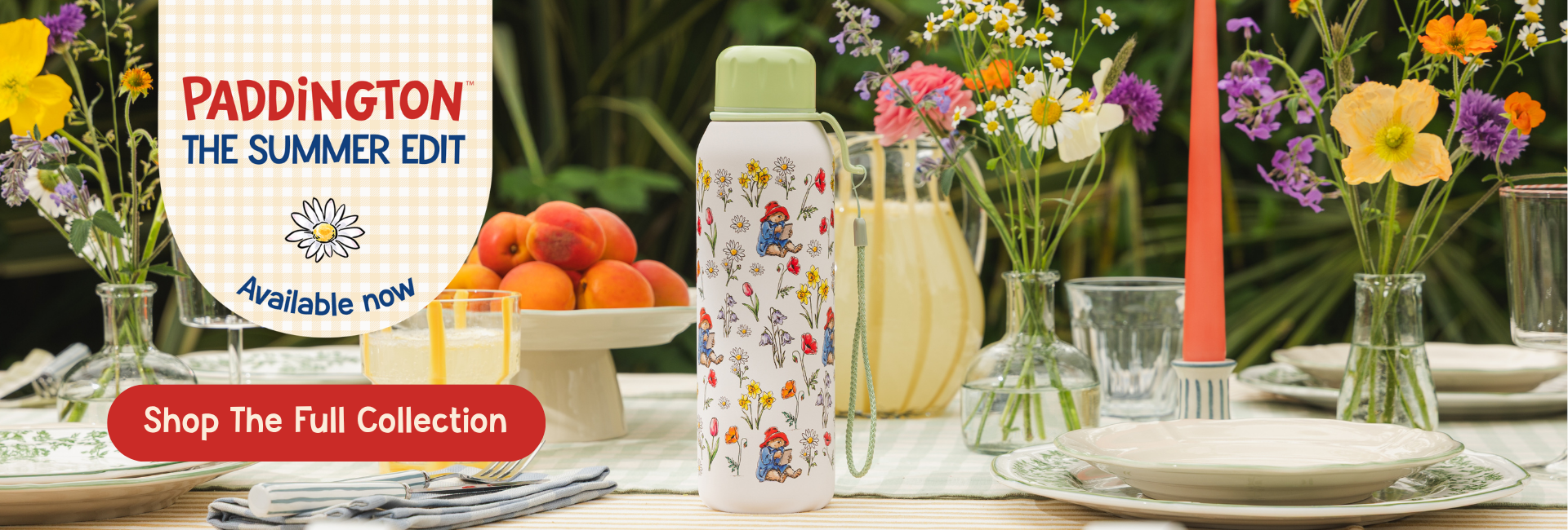 A patterned water bottle with a green lid stands on a decorated outdoor dining table surrounded by flowers, plates, and fruit. A promotional badge on the left reads 'PADDINGTON THE SUMMER EDIT' and 'Available now' with a 'Shop The Full Collection' button.