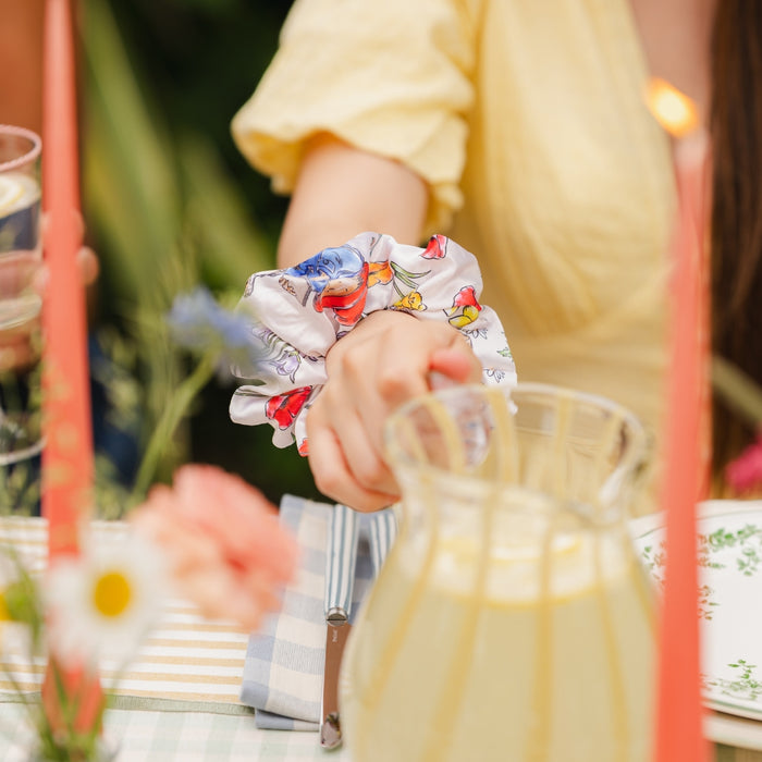 Person wearing a floral paddington bear scrunchie with a blurred background of a table setting.
