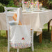 White tote bag with floral trim on a chair in front of a decorated outdoor table.