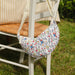 Floral-patterned crossbody Paddington bear bag attached to a chair outdoors on grass