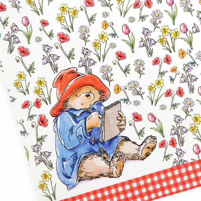 Illustration of a bear in a red hat and blue coat reading a book among flowers with a red checkered gingham border.