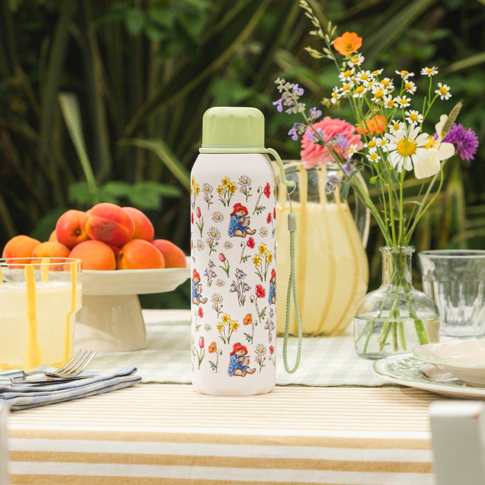 Floral-patterned water bottle on a table with fruits, flowers, and glasses.