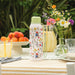 Floral-patterned water bottle on a table with fruits, flowers, and glasses.