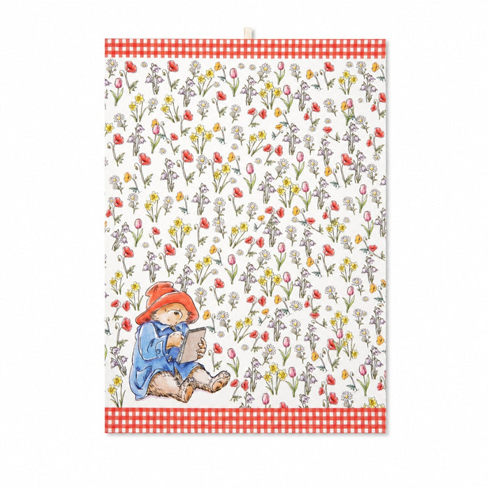 Tea towel with a Paddington writing in a book surrounded by flowers on a white background