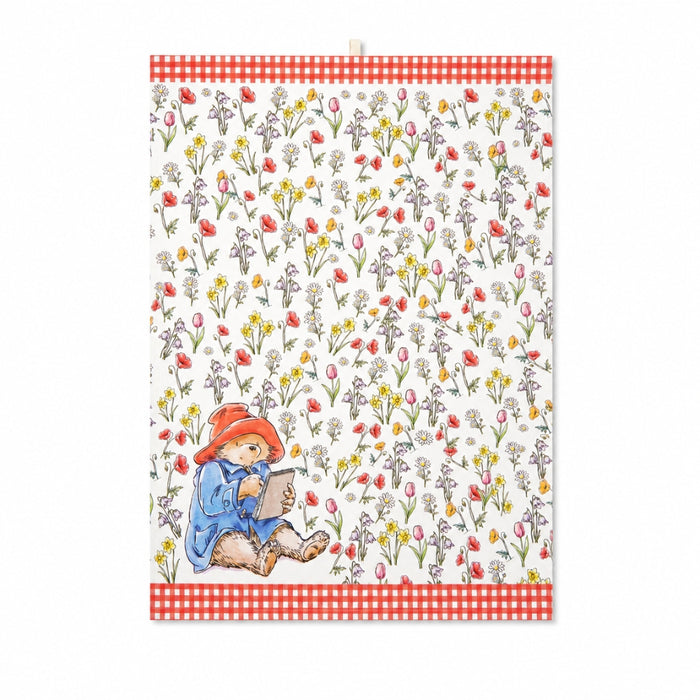 Tea towel with Paddington bear writing a book surrounded by flowers on a white background