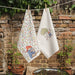 Two Paddington bear tea towels hanging on a line against a brick wall with plants.