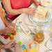 Children playing with toys at a table with a plate of sandwiches and a jar of Paddington marmalade.