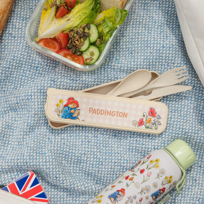 Paddington Bear-themed cutlery set with a salad and water bottle on a blue textured surface.