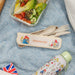 Paddington Bear-themed cutlery set with a salad and water bottle on a blue textured surface.
