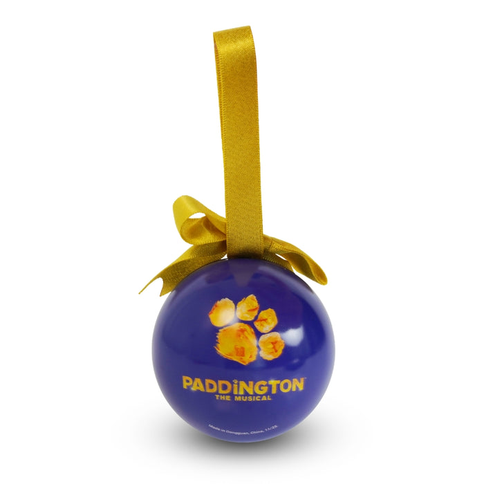 A round blue Paddington The Musical hanging Christmas ornament with a gold ribbon loop and bow, featuring the Paddington The Musical pawprint logo and title on a white background.