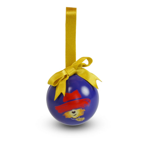 A blue Christmas ornament shaped like a ball with a yellow hanging ribbon and bow. The ornament features the  Paddington Bear Musical logo wearing a red hat.