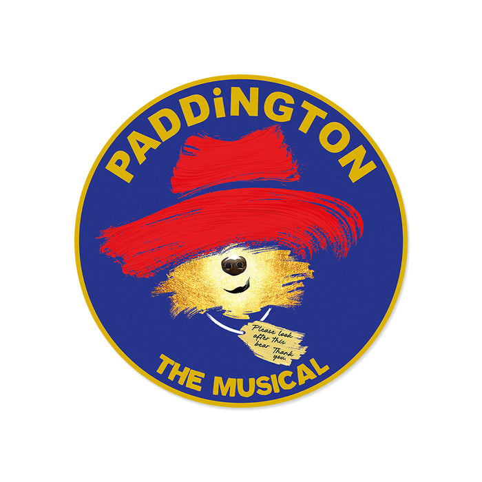 Circular logo for 'Paddington the Musical' with a bear wearing a red hat on a blue background.