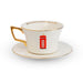 A white porcelain teacup and saucer set with gold trim, featuring a red British telephone booth illustration on the front and gold text inside the rim.