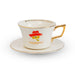 A white porcelain teacup and saucer set with gold trim, featuring a red hat illustration and the text 'PADDINGTON THE MUSICAL' on the front, set against a plain white background.