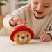 A toddler playing with a A round Paddington bear plush toy with golden-brown fur wearing a bright red hat with a yellow band, laying on a carpet