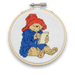 A mini cross stitch kit featuring Paddington Bear in a blue coat and red hat, sitting and writing a letter.