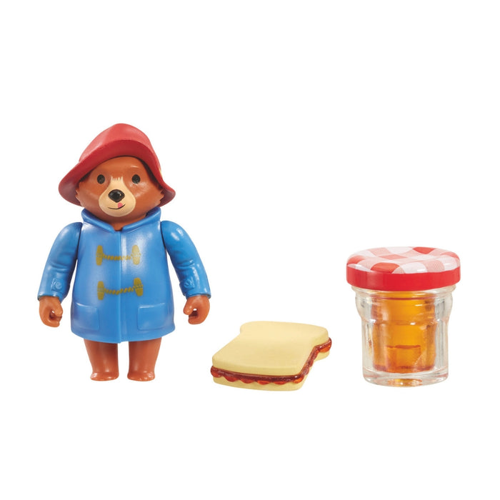 Toy figure of a bear in a blue raincoat with a jar of honey and a sandwich on a white background