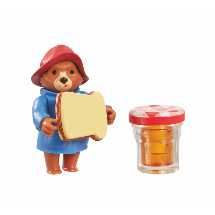 Paddington Bear toy holding a sandwich next to a jar of honey on a white background
