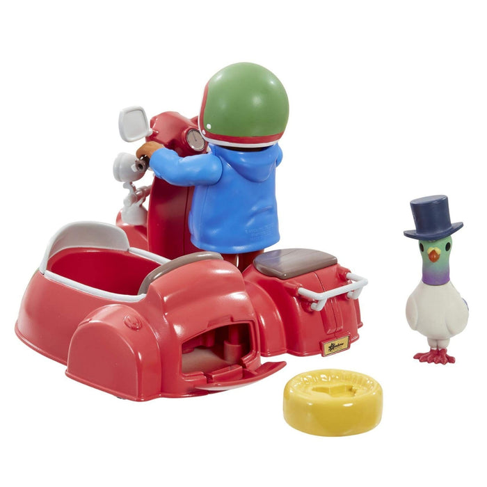 A small toy set featuring a red sidecar-style vehicle with a Paddington wearing a green helmet and blue jacket, plus a separate white goose figure with a dark top hat and a yellow ring-shaped accessory on a plain white background.
