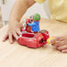 A child's hands play with a red Paddington toy scooter and sidecar set on a light wood table, with a person in a yellow shirt visible in the background.
