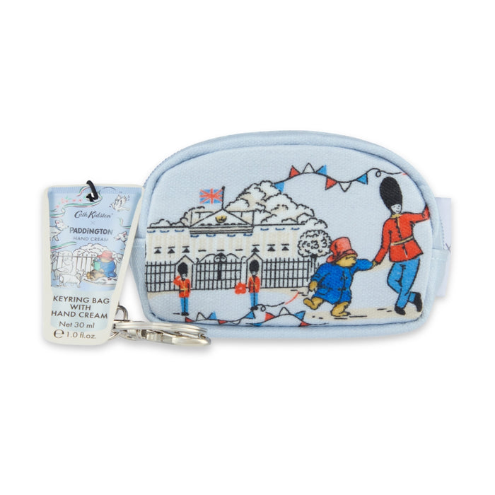 A light blue keyring bag featuring an illustration of Paddington Bear in front of Buckingham Palace, with a silver metal keyring and a hanging product tag.