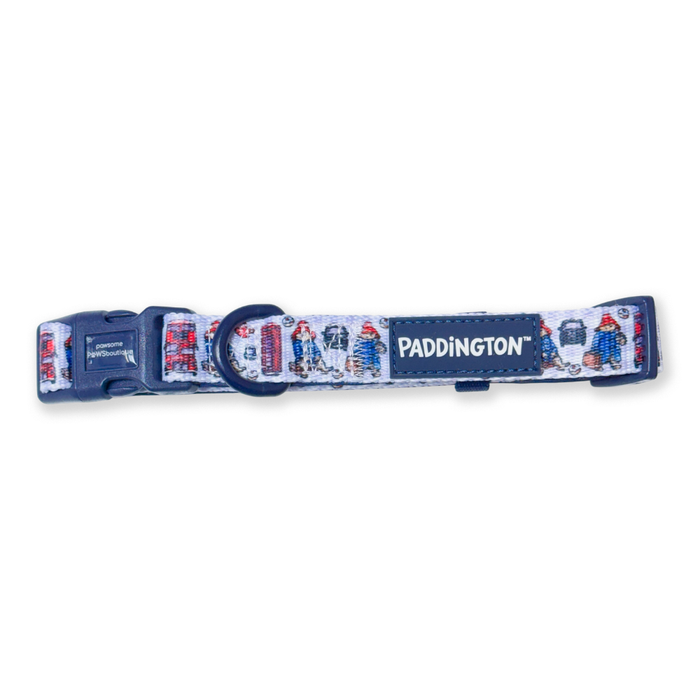 A Paddington-themed dog collar featuring a white background printed with red and blue London taxi cabs and characters, finished with a navy blue buckle and a navy blue brand label.