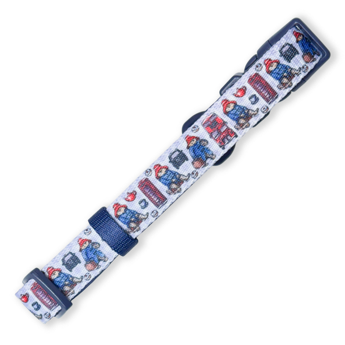 A dog collar featuring a repeating pattern of Paddington Bear and red london buses on a white background, with navy blue trim and a matching navy buckle.
