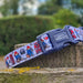 A close-up of a dog collar with a blue plastic buckle and a patterned fabric strap featuring Paddington Bear illustrations, resting on a stone ledge outdoors.