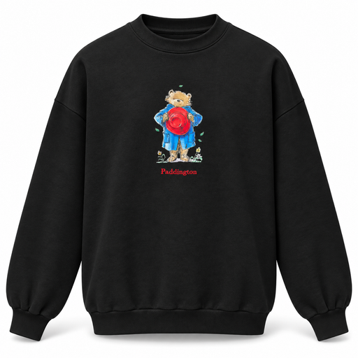 A black crewneck sweatshirt featuring a central graphic of a Paddington bear wearing a blue raincoat and holding a red bucket hat, with the word 'Paddington' printed in red below.