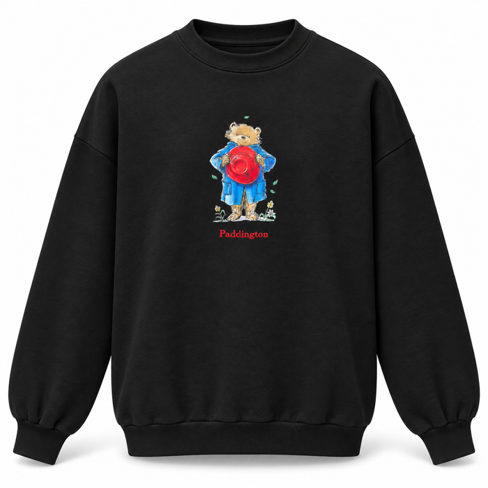 A black crewneck sweatshirt featuring a central graphic of a Paddington bear wearing a blue raincoat and holding a red bucket hat, with the word 'Paddington' printed in red below.