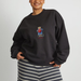 A person wearing a black crewneck sweatshirt with a small Paddington teddy bear graphic on the chest, paired with a navy and white striped knit top, against a plain light gray background.