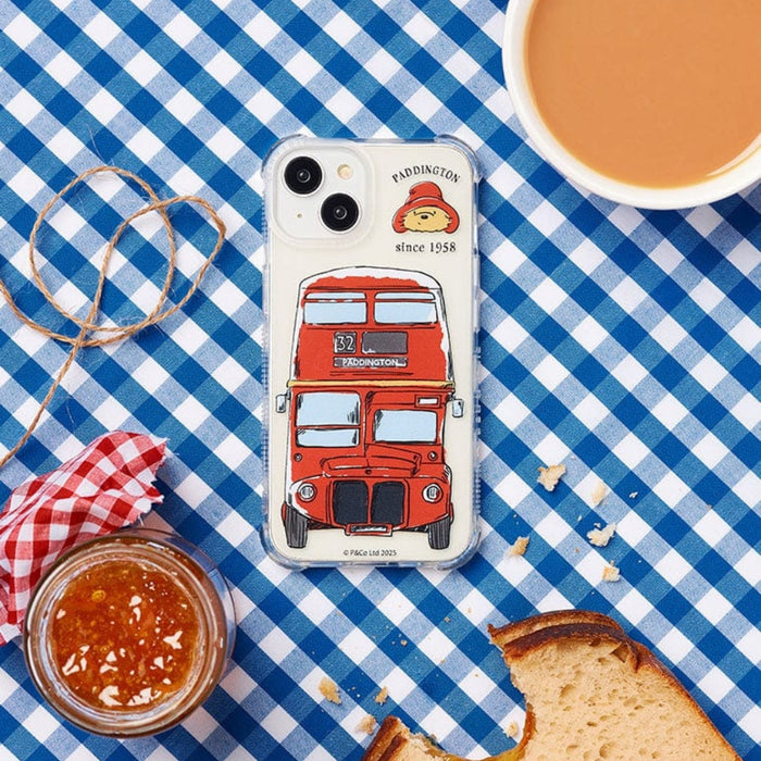 Phone case with a red bus design on a blue checkered tablecloth with a cup of coffee, jar of jam, and bread.