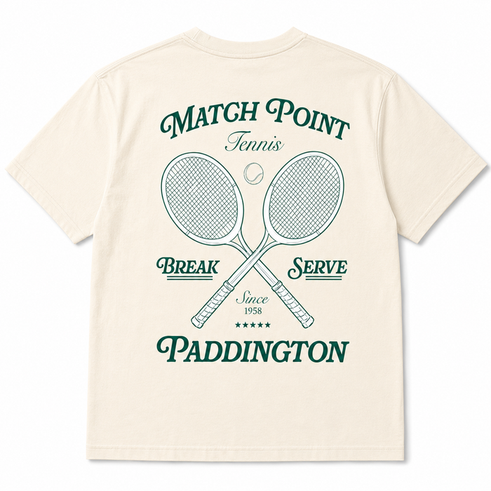An off-white short-sleeve t-shirt showing the back, which features a dark green graphic print with crossed tennis rackets, a tennis ball, and the text 'MATCH POINT Tennis BREAK SERVE Since 1958 PADDINGTON'.