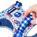 A close-up of a Paddington-themed dog harness with a blue and white gingham strap, featuring a blue brand patch and a cartoon bear print on a white background. A human hand is adjusting the strap.