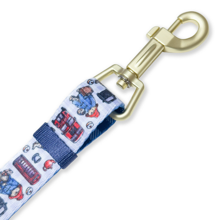 A close-up of a pet leash featuring a white woven fabric with a colorful cartoon pattern of red buses, blue cars, and characters, attached to a gold-toned metal swivel clasp.