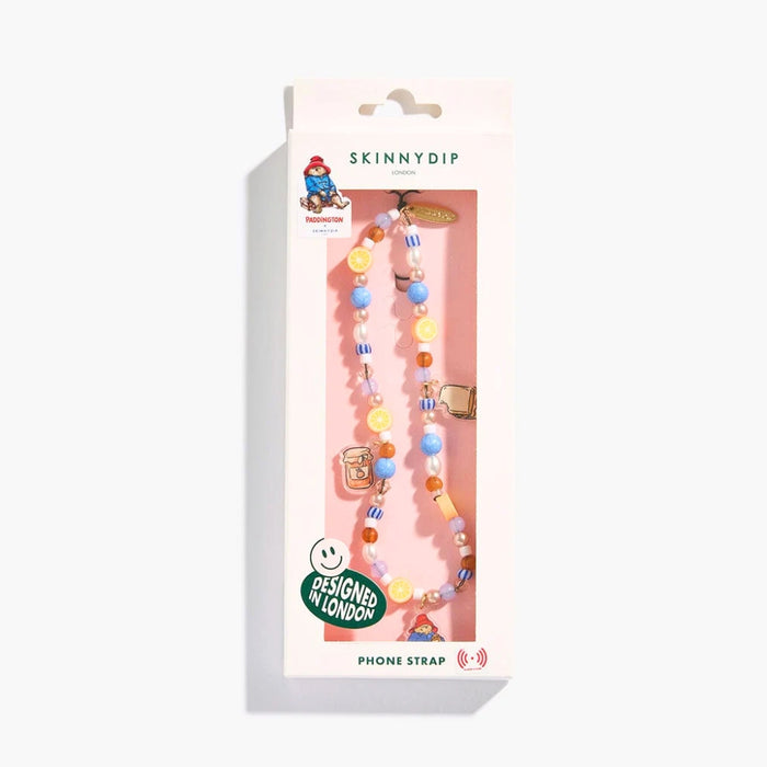 A beaded phone strap by Skinny Dip, featuring colorful round beads in blue, yellow, orange, and white, with small paddington bear charms, shown in its original pink packaging against a white background.