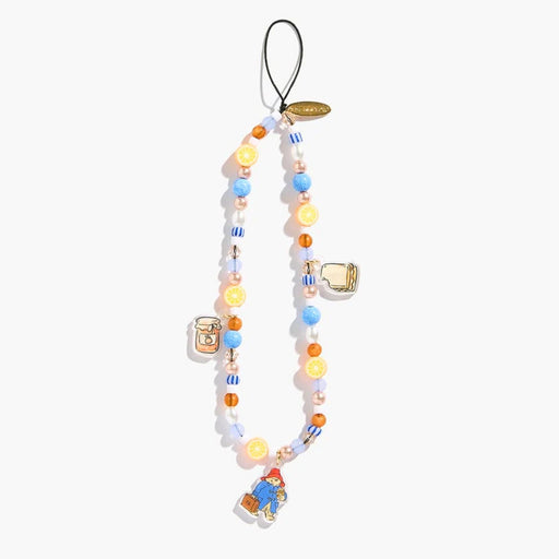 A beaded phone strap featuring pastel blue, yellow, and white beads with various paddington cartoon charms, including paddington bear carrying a suitcase, set against a plain off-white background.