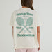 A woman viewed from the back wearing a cream-colored t-shirt with a green tennis-themed graphic print that reads 'MATCH POINT Tennis BREAK SERVE Since 1958 PADDINGTON' around two crossed tennis rackets.