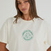A woman wearing a cream-colored crewneck t-shirt with a green circular 'Match Point Paddington' logo printed on the chest, set against a plain light background.