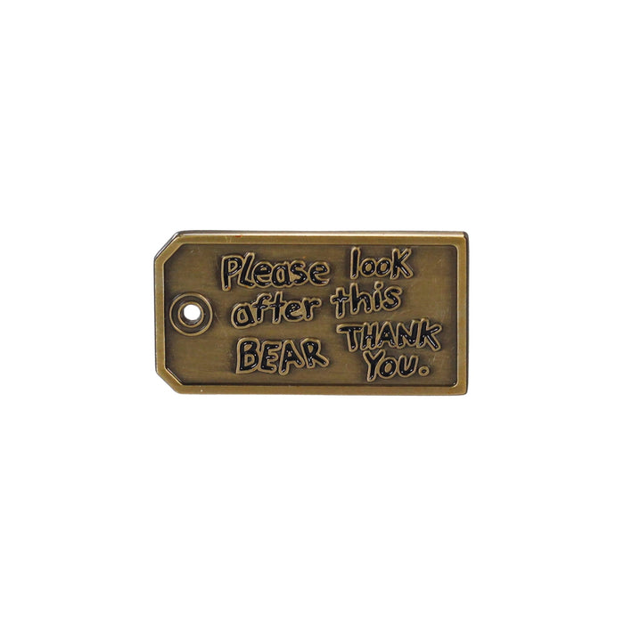 A rectangular pin badge with the text 'Please look after this bear. Thank you.' in a bronze tone.