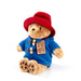 Plush toy Paddington bear wearing a red hat and blue coat with a tag on a white background