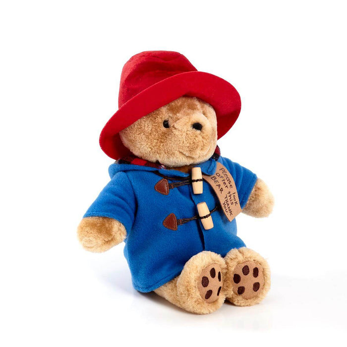 Stuffed toy Paddington bear in a blue coat and red hat on a white background