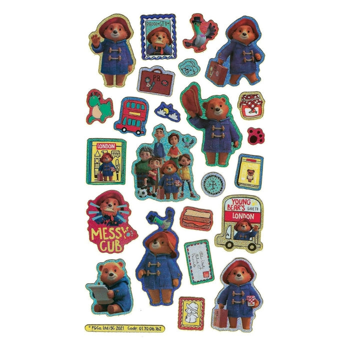 A sheet of colorful Paddington Bear themed stickers and small cutout pieces on a plain white background, including Paddington in a duffel coat, a red London bus, a suitcase, a hat, and various character illustrations.