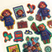 A sheet of colorful die-cut stickers featuring Paddington Bear illustrations and London-themed designs, including a large Paddington sticker, a stamp-style badge, a suitcase, a red double-decker bus, and character group scenes on a white background.