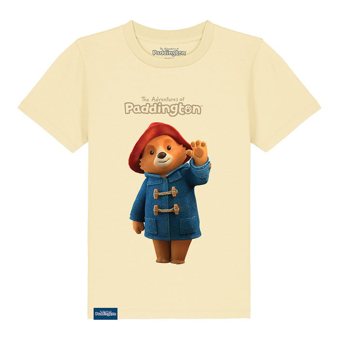 A butter cream kids' T-shirt with a graphic of Paddington Bear in a red hat and blue coat on a yellow background, with the text 'The Adventures of Paddington'.
