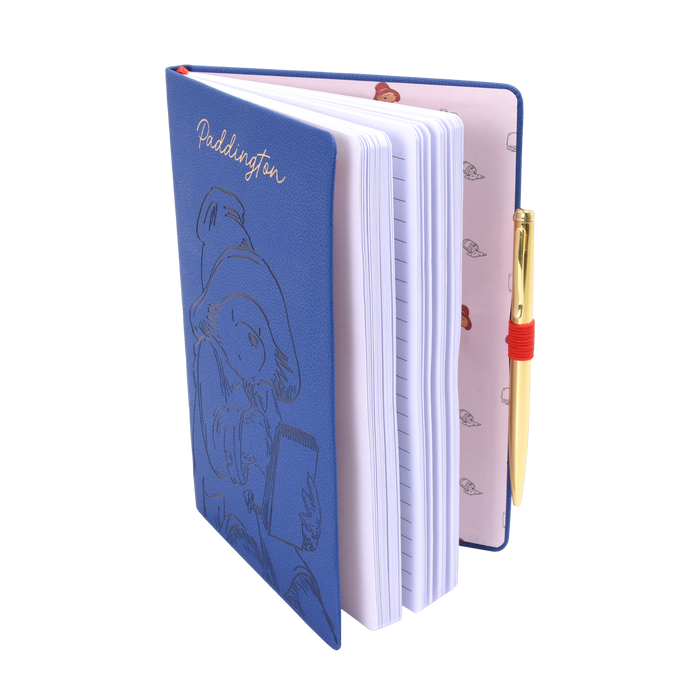 Blue notebook with a Paddington bear character design on the cover, open to reveal white pages and a gold pen.