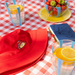 Red hat with a Paddington bear emblem on a checkered tablecloth with glasses of lemonade and a bowl of strawberries.