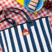 blue and white Striped tote bag with a cartoon Paddington bear character on a red and white checkered tablecloth with picnic items.