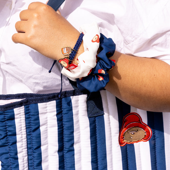 Close-up of a person's wrist with multiple scrunchies featuring cartoon Paddington bear on a striped fabric background.
