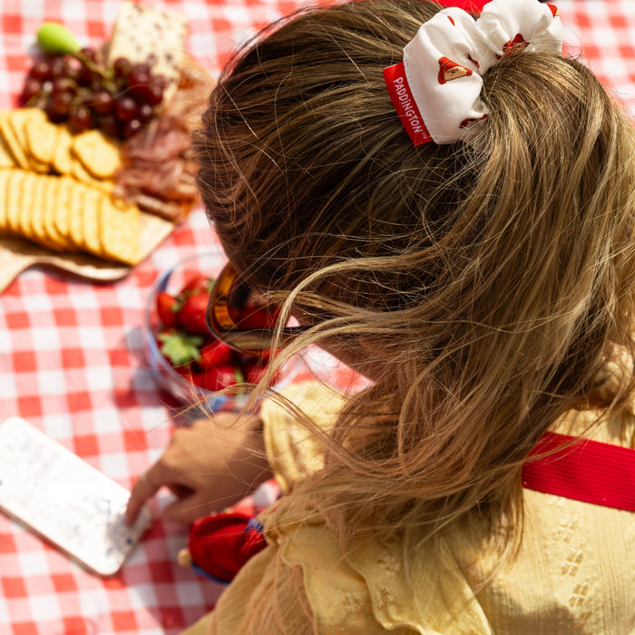 Child with a white Paddington hair scrunchie at a picnic table with food